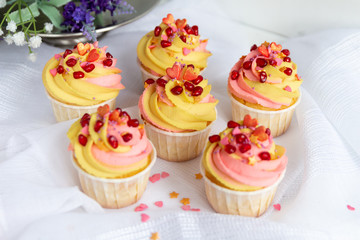  Traditional lemon cupcakes on a white background. With pink-yellow butter cream and pomegranate seeds.