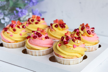 Traditional lemon muffins on a white background in a packing box. With pink-yellow butter cream and pomegranate seeds. Close-up