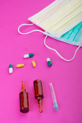 Protective face mask on pink background, pills, needle