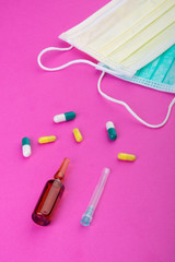 Protective face mask on pink background, pills, needle