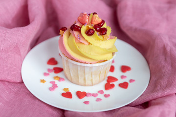  Traditional lemon cupcake on a white plate and pink background. With pink-yellow butter cream and pomegranate seeds. Close-up