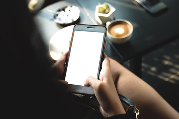 Mockup image of a woman holding and showing black mobile phone with blank screen in cafe