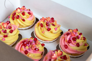Traditional lemon muffins on a white background in a packing box. With pink-yellow butter cream and pomegranate seeds. Close-up