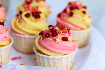  Traditional lemon cupcakes on a white background. With pink-yellow butter cream and pomegranate seeds. Close-up