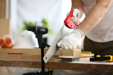 Gloved carpenter uses transverse sawing fixed part - obrazy, fototapety, plakaty