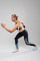 Fototapeta premium slim fit blonde girl in a sports uniform is engaged in physical exercises on a gray background