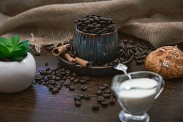 cup full of coffee beans with plant, bun and milk on brown table