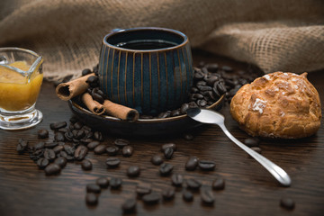 cup of coffee with cinnamon sticks, orange jam and bun on brown table