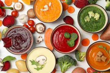 Vegetable soups and ingredients on white wooden background, top view