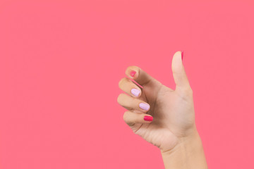 Closeup view photography of one manicured beautiful female hand making gesture by empty hand as if holding invisible object in palm isolated on bright pink background.