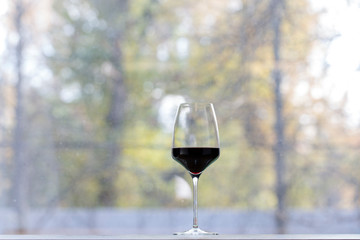 One wine glass with the red wine on a sill.