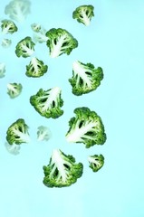 Flying green broccoli slices on a blue background. Concept of flying food, green vegetables, diet food, veggies pattern. Copy space for text.