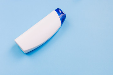 Cosmetic bottle without a label on a blue background. Plastic jar with a blue lid. Shampoo or hair lotion. Top view, copy space.