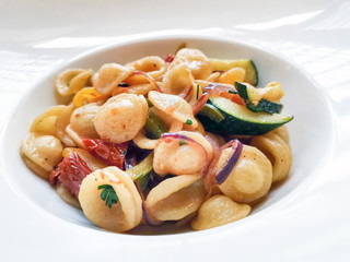 Vegetarian pasta cooked with mixture of vegetables, like zucchini, red and green pepper, onion and dried tomatoes served in white plate