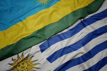 Obraz premium waving colorful flag of uruguay and national flag of rwanda.
