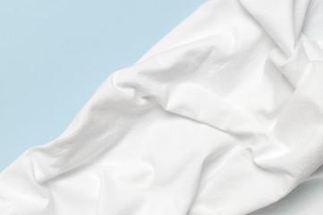 White crumpled natural cotton fabric on delicate blue background top view flat lay with copy space....