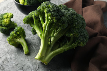 Broccoli, board and towel on grey background, close up. Healthy food