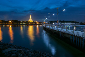 Fototapeta na wymiar Beautiful lighting of Bridge across buangkaennakorn lake with background of Wat Nong Wang temple and reflection on the water at twilight ,Khonkaen province,Thailand