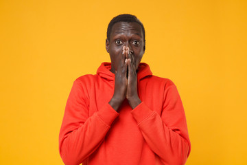 Shocked young african american man guy in red streetwear hoodie posing isolated on yellow orange background studio portrait. People lifestyle concept. Mock up copy space. Covering mouth with hands.