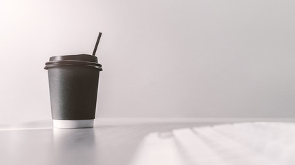 take away paper cup of hot coffee with computer keyboard on top of wooden working table in morning sunlight