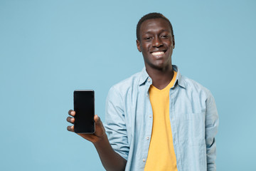 Smiling young african american man guy in casual shirt, yellow t-shirt posing isolated on blue wall background. People lifestyle concept. Mock up copy space. Hold mobile phone with blank empty screen.