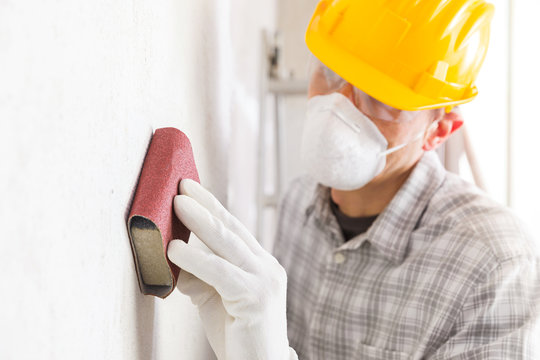 Plasterer or painter sanding a white wall