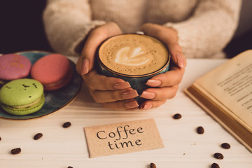 Beautiful female hands hold a blue cup with coffee. The girl is sitting at the table in the cafe....