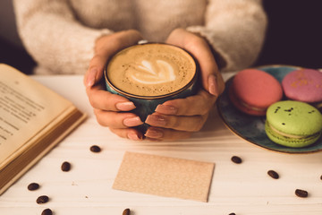 Beautiful female hands hold a blue cup with coffee. The girl is sitting at the table in the cafe....