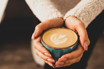 Beautiful female hands holding a blue cup with cappuccino.