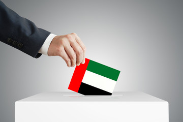 Man putting a voting ballot into a box with United Arab Emirates flag.