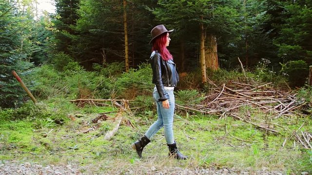 Red-haired woman in a jacket walks along a forest path in side view