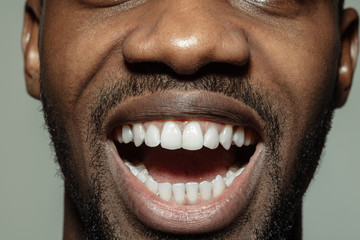 Scretching, teeth showing. Close up of face of beautiful african-american young man, focus on mouth. Human emotions, facial expression, cosmetology, body and skin care concept. Well kept skin
