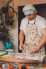A man dressed in an apron and hat prepares dumplings in the kitchen.