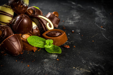 Various chocolate candies over dark background. Different sweet and chocolates with mint leaves, copy space