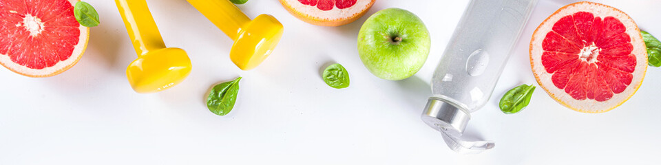Fitness and healthy food lifestyle concept. Dumbbells, diet fruit and vegetable lunch box, water and jump rope on white background. Flatlay image, top view copy space