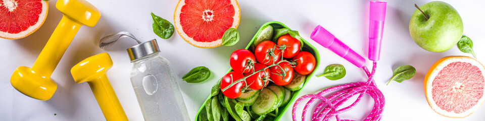 Fitness and healthy food lifestyle concept. Dumbbells, diet fruit and vegetable lunch box, water and jump rope on white background. Flatlay image, top view copy space