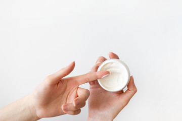 Girl finger applying moisturizer cream in white plastic container on white background. Daily routine skincare and bodycare, top view