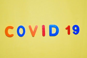 COVID-19 written in various colored letter blocks on a light yellow background