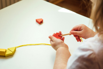 Child putting beads on a string. Bead stringing activity. Fine motor skills development. Lacing, threading.