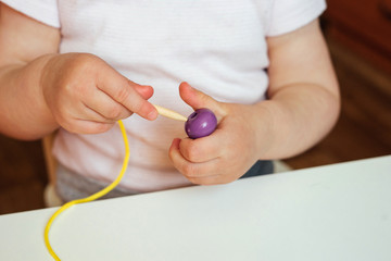 Child putting beads on a string. Bead stringing activity. Fine motor skills development. Lacing, threading.