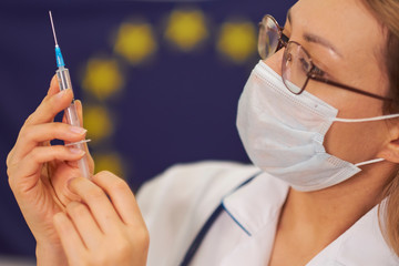 doctor is standing against the background of the European Union flag. in the hands of a syringe in the vaccine. Novel coronavirus 2019-nCoV