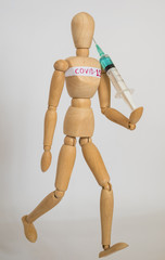 COVID-19 Pandemic Coronavirus concept ; Close-up of a wooden model man is carrying syringe. Corona virus vaccine on the way. 
