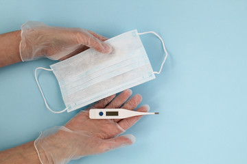 Hands in gloves hold medical mask and thermometer on a blue background