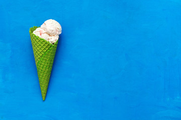Ice cream in a green waffle cone on a blue background, flat lay. Top view, copy space. Summer refreshing dessert.