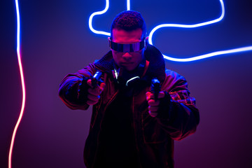 selective focus of mixed race cyberpunk player in futuristic glasses holding guns near neon lighting