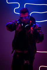 handsome mixed race cyberpunk player in futuristic glasses holding gun near neon lighting