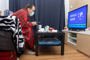 The sick man with remote control in hand watching TV news about global virus attack. A home treatment in quarantine.