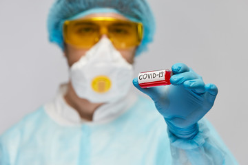laboratory doctor in safety biohazard suit holding COVID-19 antivirus in arm with blue gloves