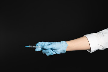 Female doctor hands with syringe on dark background close up.