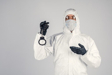 Fototapeta na wymiar A man in a white chemical protective suit with handcuffs in his hands. An epidemic pandemic is a new rapidly spreading virus, a medical concept. Lack of freedom during the virus.